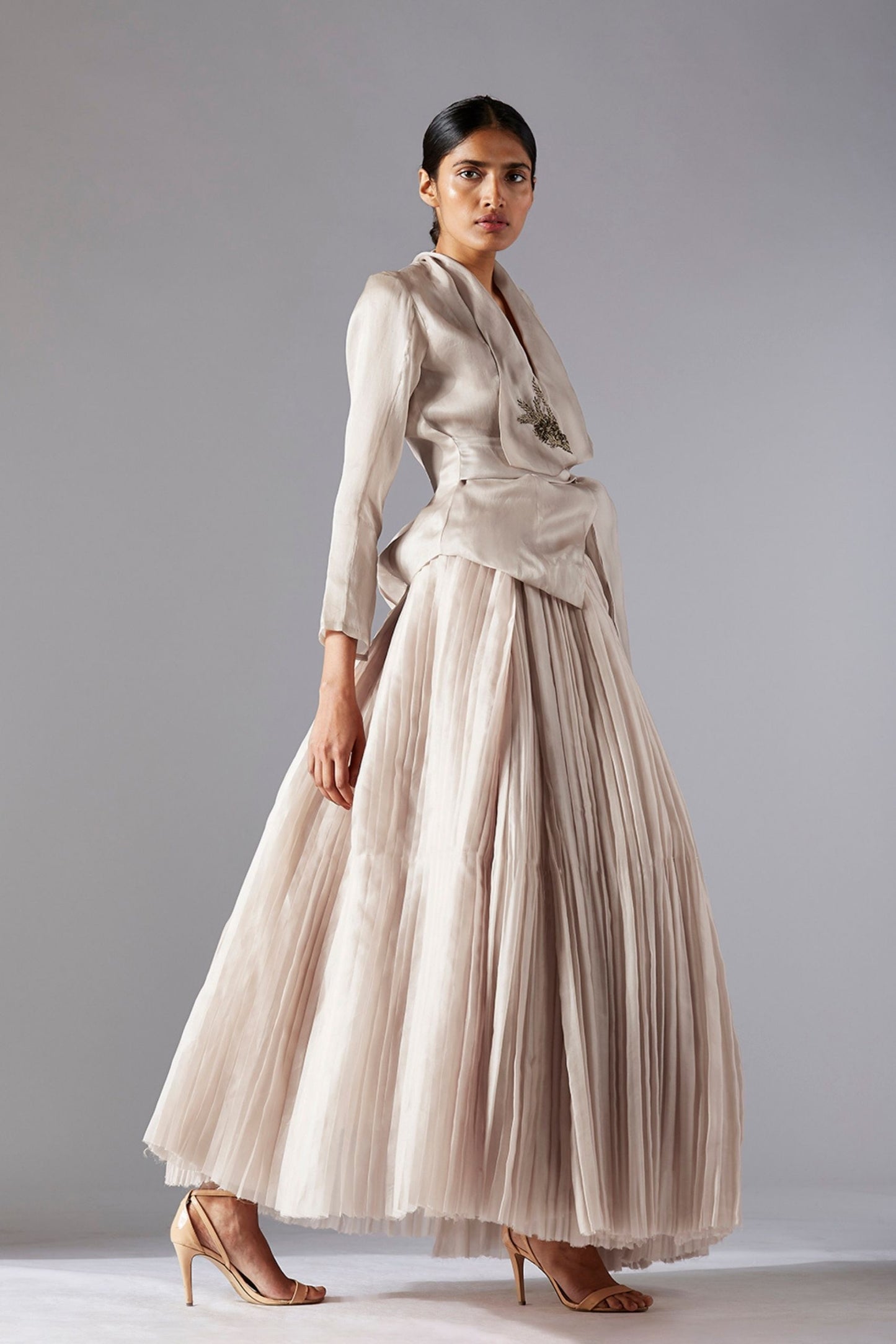 Side profile of a woman showcasing the elegant silhouette created by the designer organza jacket and pleated skirt