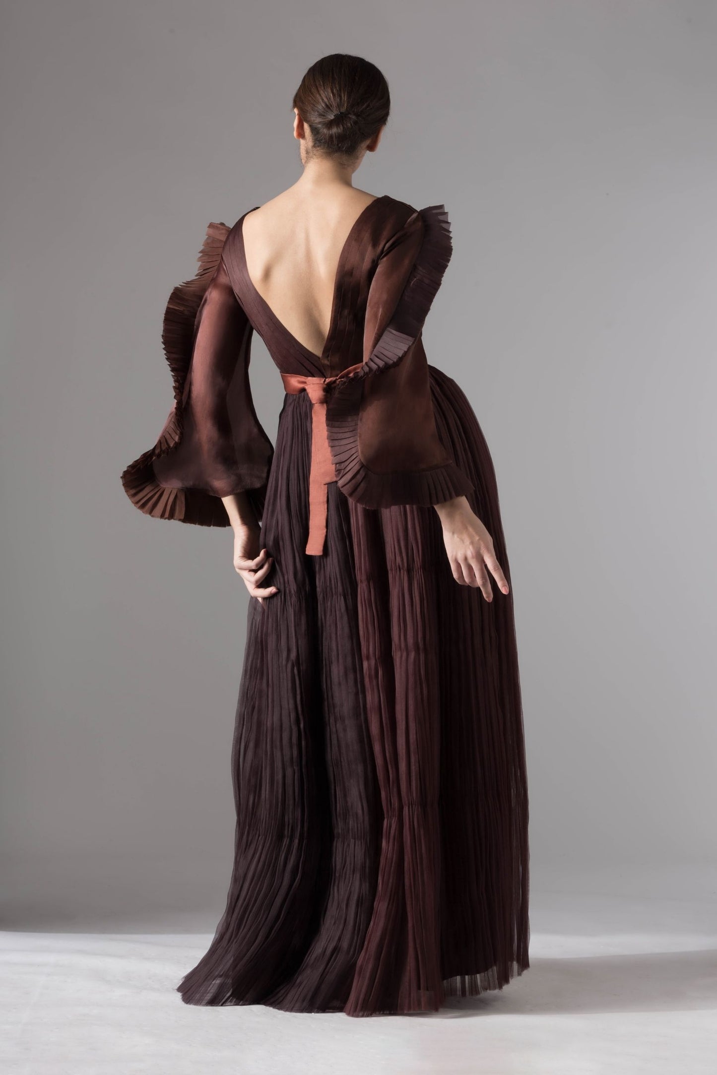 Back view of the evening gown, focusing on the sleek fit, pleated ruching, and rope-inlay belt detailing