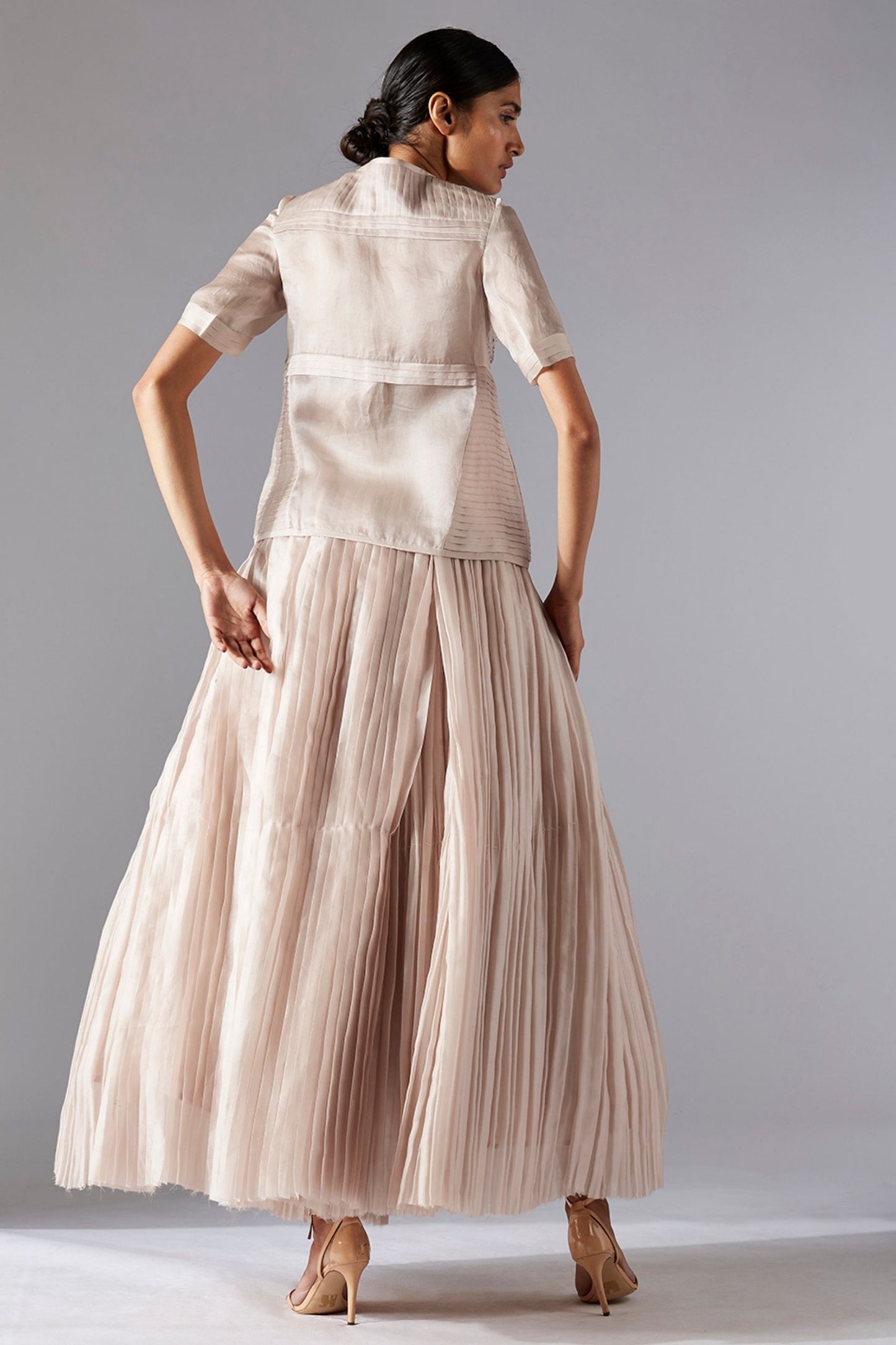 Back view highlighting the flow of the pleated ballroom skirt and the detailed design of the sheer geometric jacket